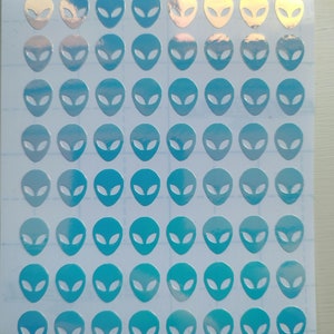 May include: A sheet of holographic alien head stickers in shades of blue. The stickers are arranged in a grid pattern on a white background.