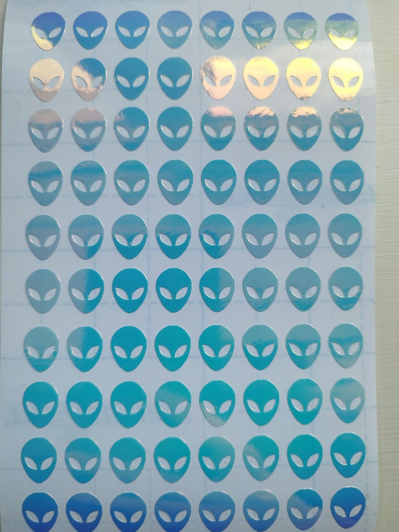 May include: A sheet of holographic alien head stickers in shades of blue. The stickers are arranged in a grid pattern on a white background.