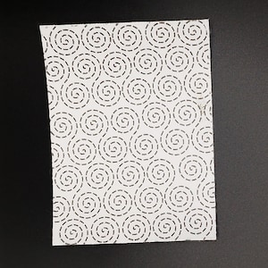 A rectangular sashiko pattern on a black background. The pattern has a swirling dashed line design.