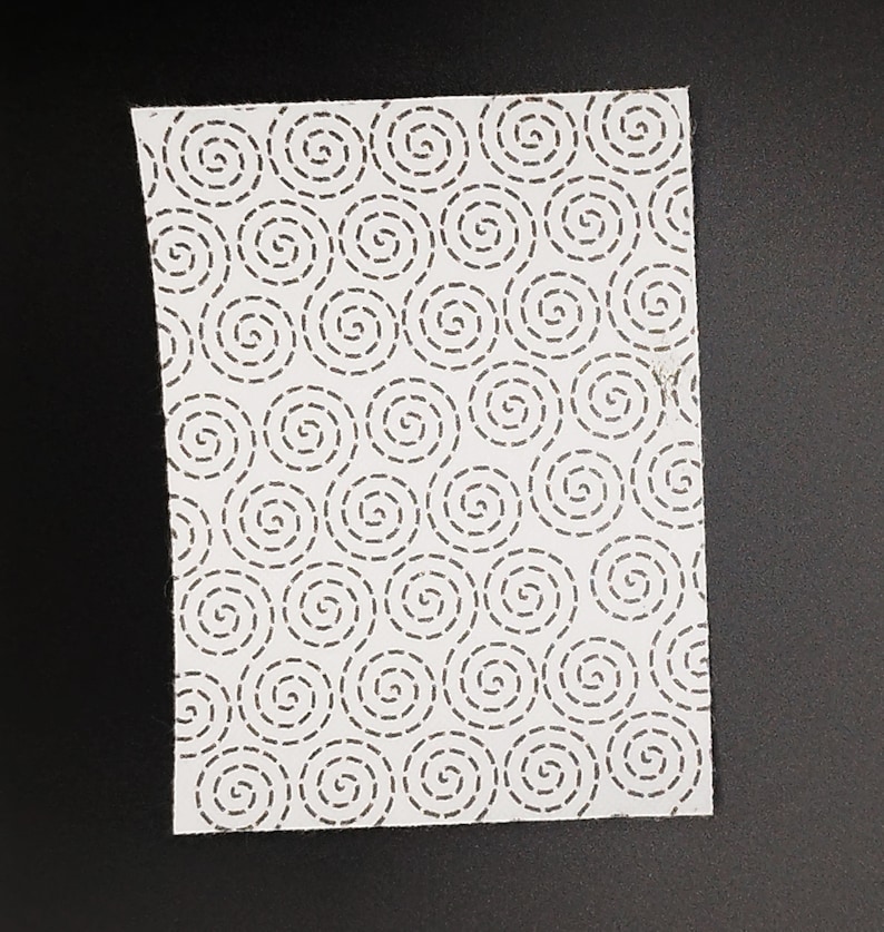 A rectangular sashiko pattern on a black background. The pattern has a swirling dashed line design.