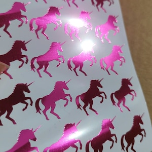 Könnte beinhalten: Eine Bogen mit pinken holografischen Einhorn-Aufklebern. Die Einhörner sind nach rechts gerichtet und haben ein einzelnes Horn.