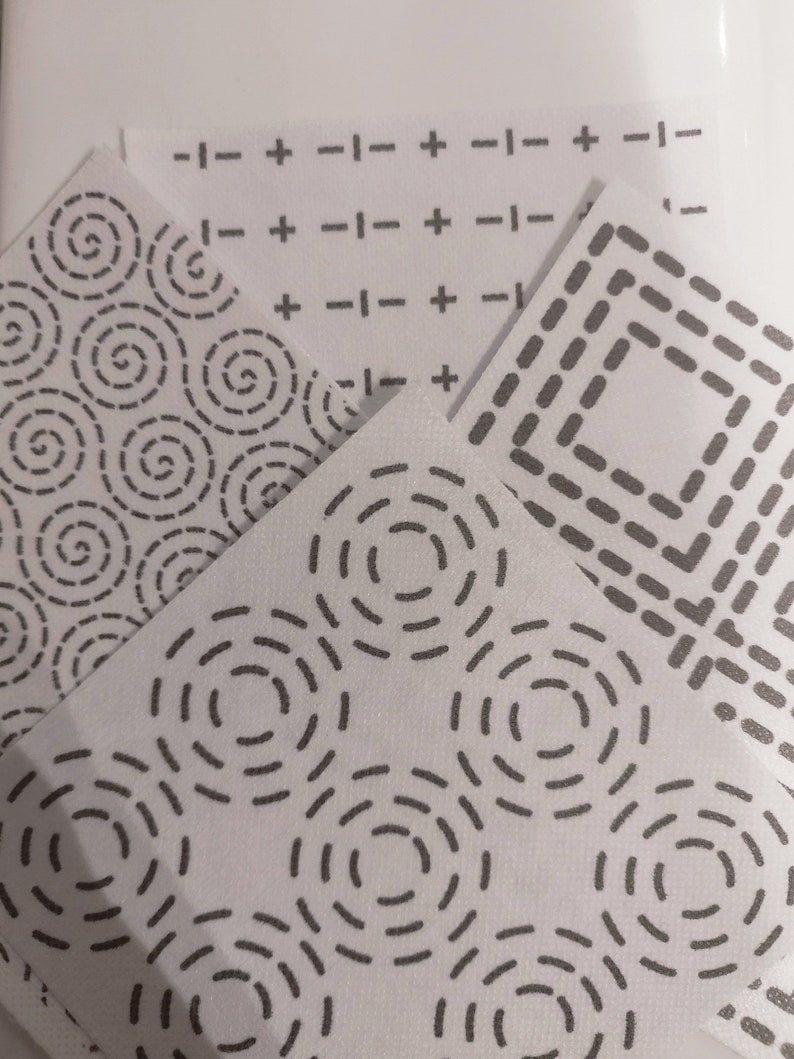 4 Sashiko Transfers. In the foreground is a concentric circles pattern. On the right is a concentric square pattern. At the back is a crosses and dashes sashiko pattern. On the left is a swirls dashed sashiko pattern
