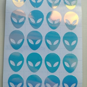 May include: A sheet of 18 iridescent blue alien head stickers. The stickers are arranged in a grid pattern on a white sheet.