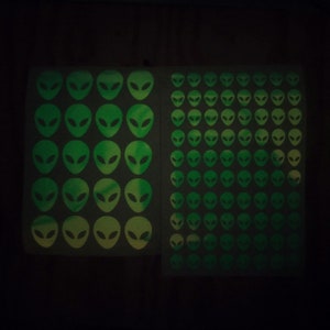 May include: Two sheets of glow-in-the-dark stickers featuring green alien faces. The stickers are arranged in a grid pattern.