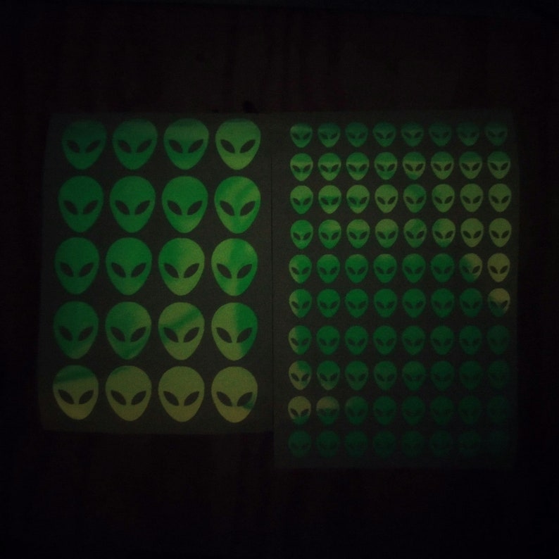 May include: Two sheets of glow-in-the-dark stickers featuring green alien faces. The stickers are arranged in a grid pattern.