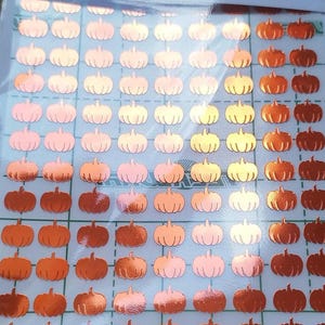 May include: Sheet of pumpkin-shaped stickers in shades of orange, peach, and gold. The stickers are arranged in a grid pattern, ideal for autumn crafts and decorations. The stickers are on a clear backing.