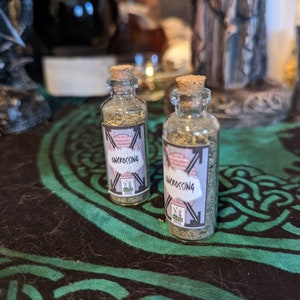 Könnte beinhalten: Zwei kleine Glasflaschen mit Korkverschlüssen, gefüllt mit getrockneten Kräutern. Die Flaschen haben schwarze und weiße Etiketten mit dem aufgedruckten Wort "Uncrossing".