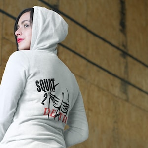 May include: A white hooded sweatshirt with the text "SQUAT 2 DEATH" printed on the back in black and red. The graphic includes a skeleton hand and a stylized buttock design. The sweatshirt is made of a soft material.
