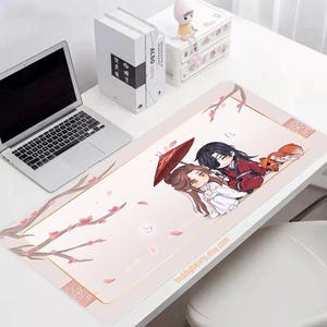 Puede incluir: Alfombrilla de ratón rectangular rosa con una ilustración de estilo anime de dos personajes bajo un paraguas rojo, con un zorro. La alfombrilla tiene un diseño floral y el texto "beddigitalarts.etsy.com".