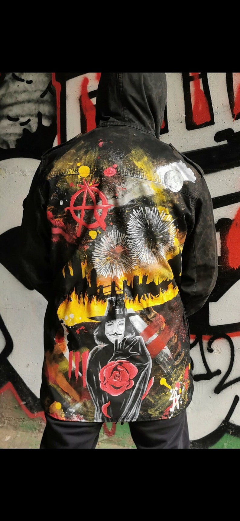 May include: A black jacket with a colorful, abstract design featuring a red rose, a figure wearing a mask, and a symbol resembling an anarchy sign. The design also includes yellow flames and white fireworks.