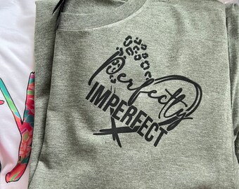 May include: A green t-shirt with a black heart design and the text "Perfectly Imperfect" printed on the front.