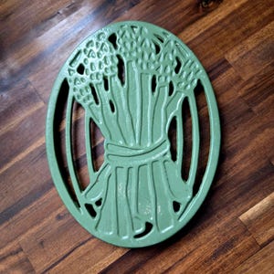 May include: Green cast iron trivet shaped like a bunch of asparagus. The trivet has a raised design and is perfect for protecting surfaces from hot dishes.