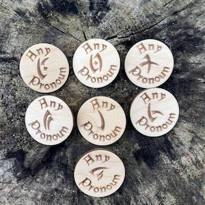May include: Seven wooden tokens with the text "Any Pronoun" and different symbols on each. The tokens are on a wooden surface.