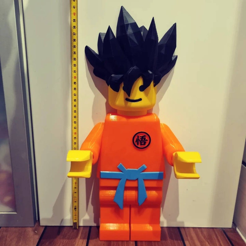 Op de afbeelding: Een groot, oranje en geel Lego-figuur van een personage met zwart stekelig haar. Het figuur draagt een blauwe riem en heeft een rode cirkel op de borst met het Japanse karakter "悟" (Go) erin.