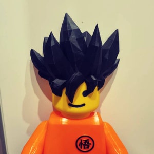 Op de afbeelding: Een zwart en oranje Lego-figuur met stekelig zwart haar en een geel gezicht. Het figuur heeft een zwart kanji-teken op zijn borst dat "悟" leest.