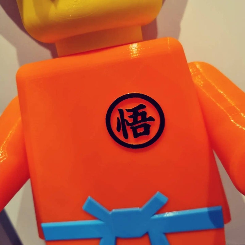 Op de afbeelding: Oranje en gele Lego-figuur met een zwarte cirkel op de borst waarop in zwarte kanji "悟" staat.