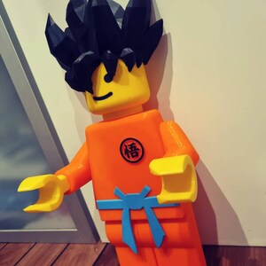 Op de afbeelding: Een groot, oranje en geel Lego-figuur met zwart stekelig haar. Het figuur draagt een blauwe riem en heeft een kanji-teken op de borst.