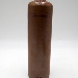 May include: A brown stoneware bottle with a rounded bottom and a narrow neck. The bottle has a faint blue glaze and a small brown stamp on the bottom that reads "6K021".