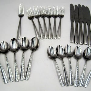 May include: A set of silverware, including forks, spoons, and knives, all made of stainless steel. The silverware is arranged in rows on a white surface.