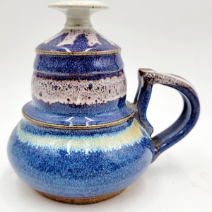May include: A blue and white ceramic teapot with a handle and a lid. The teapot has a speckled glaze and a unique design.