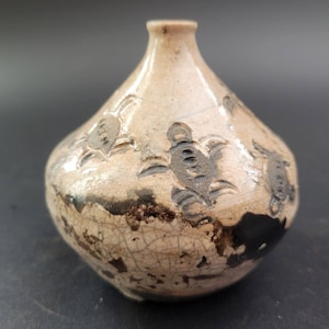 May include: A small, round, white ceramic vase with a brown glaze and a crackled finish. The vase is decorated with black painted images of turtles.