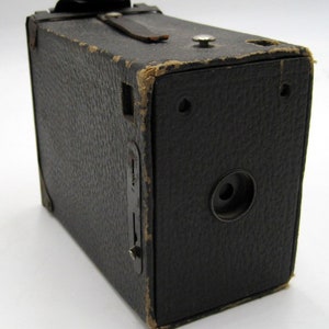 May include: A black vintage box camera with a leather strap and a lens on the front.