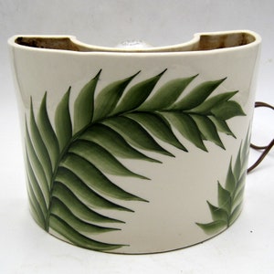 May include: A white ceramic lamp with a green palm leaf design. The lamp has a cord and a switch.