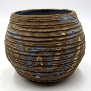 May include: A brown ceramic pot with blue and white paint accents. The pot has a rounded shape and a textured surface.