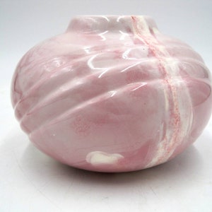 May include: A pink ceramic vase with a swirl design and white accents. The vase has a round shape and a smooth, glossy finish.