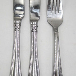 May include: A set of three silver-toned cutlery pieces, including a fork and two knives. The handles are decorated with a floral design and the word "ONEIDA" is engraved on the knives.