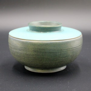 May include: A ceramic bowl with a lid, both glazed in a light blue and green color. The bowl has a rounded shape and a slightly flared rim. The lid has a small knob on top.
