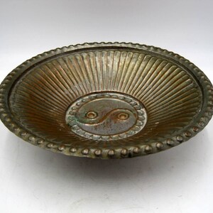 May include: A round, metal bowl with a textured, sunburst design. The bowl has a raised, circular design in the center featuring a yin yang symbol.