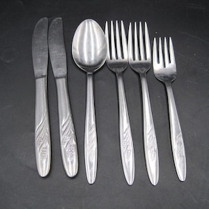 May include: Set of six silver-toned flatware with floral designs on the handles. The set includes two butter knives, one spoon, and three forks.
