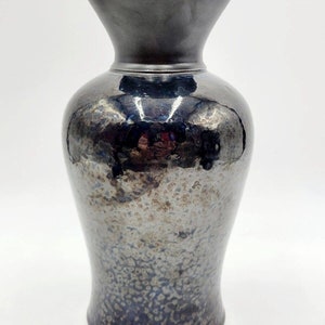 May include: A dark blue ceramic vase with a textured, speckled glaze. The vase has a wide, flared opening and a narrow base.