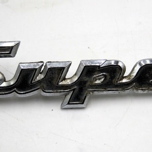 May include: A chrome and black metal emblem with the word "Super" embossed on it.