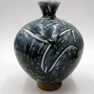 May include: A small, round ceramic vase with a narrow neck. The vase is decorated with a blue and white glaze, with white lines and dots on a dark blue background.