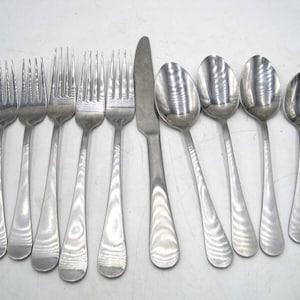 May include: A set of stainless steel silverware, including forks, knives, and spoons. The silverware has a simple, elegant design with a polished finish. The forks have four tines, and the spoons have a rounded bowl. The knife has a smooth, rounded blade.