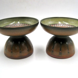 May include: Two ceramic bowls with a brown and green glaze. The bowls have a raised base with a decorative design.