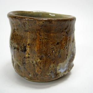 May include: A brown ceramic cup with a textured surface. The cup has a wide rim and a rounded base.