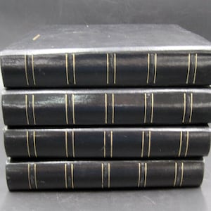 May include: Five black leather-bound books with gold accents stacked on top of each other.