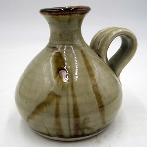 May include: A small, light green ceramic pitcher with a brown rim and a brown glaze. The pitcher has a round body and a single handle.