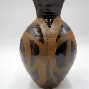 May include: A brown and tan ceramic vase with a wide base and a narrow neck. The vase has a unique design with brown and tan swirls.
