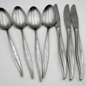 May include: Set of six stainless steel silverware, including four spoons and two knives. The silverware has a brushed finish and a curved handle.