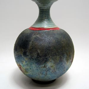 May include: A dark blue ceramic vase with a textured surface and a white and red rim. The vase has a narrow neck and a round body.