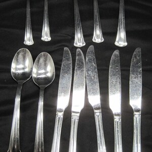 May include: A set of silverware, including forks, spoons, and knives, all made of polished stainless steel. The silverware is arranged in a row on a black surface.