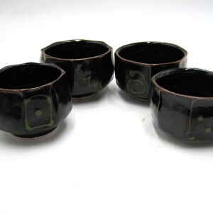 May include: Four black ceramic bowls with green and white geometric designs. The bowls are slightly irregular in shape and have a glossy finish.