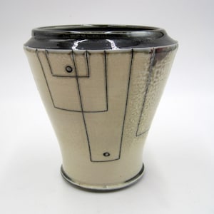 May include: A white ceramic vase with a geometric design in black. The vase has a wide mouth and a narrow base.