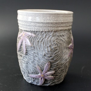 May include: A ceramic mug with a textured, gray surface and a white rim. The mug is decorated with three pink flowers.