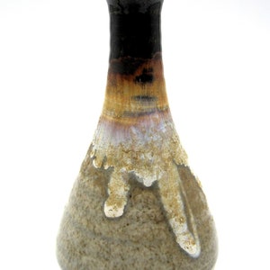 May include: A small, brown and white ceramic vase with a narrow neck and a wide base. The vase has a drip glaze effect, with white and brown glaze running down the sides.