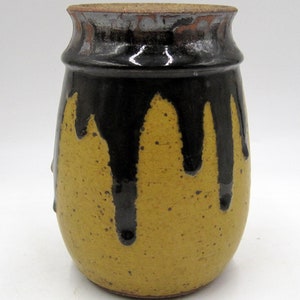 May include: A yellow ceramic vase with black glaze dripping down the sides. The vase has a rounded body and a slightly flared opening.